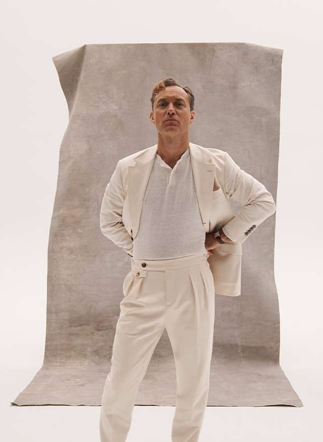 Portrait of a man in a cream-colored suit posing in front of a textured backdrop. He is fair-skinned with light brown hair.