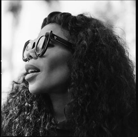 Black and white portrait of a woman wearing statement sunglasses and voluminous curly hair by photographer Paola Kudacki.