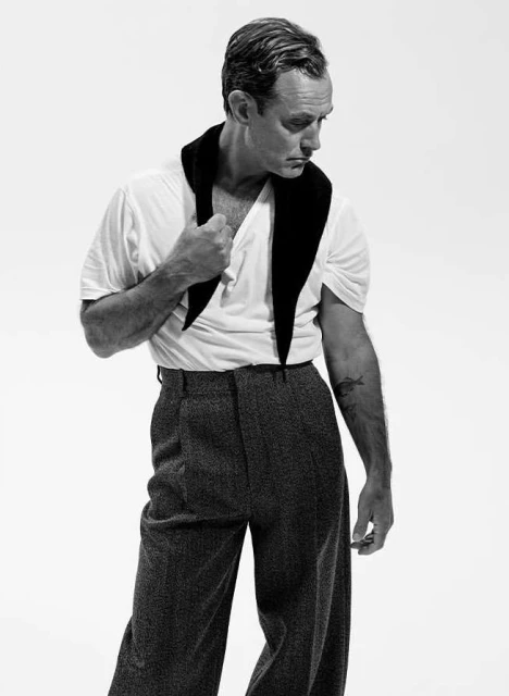 Monochrome portrait of adult male in a white t-shirt and grey slacks, accessorized with a black scarf. He glances off-camera against a plain white backdrop.