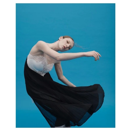 Model in a black and white dress with lace trim posing against a solid blue background by photographer Paola Kudacki.