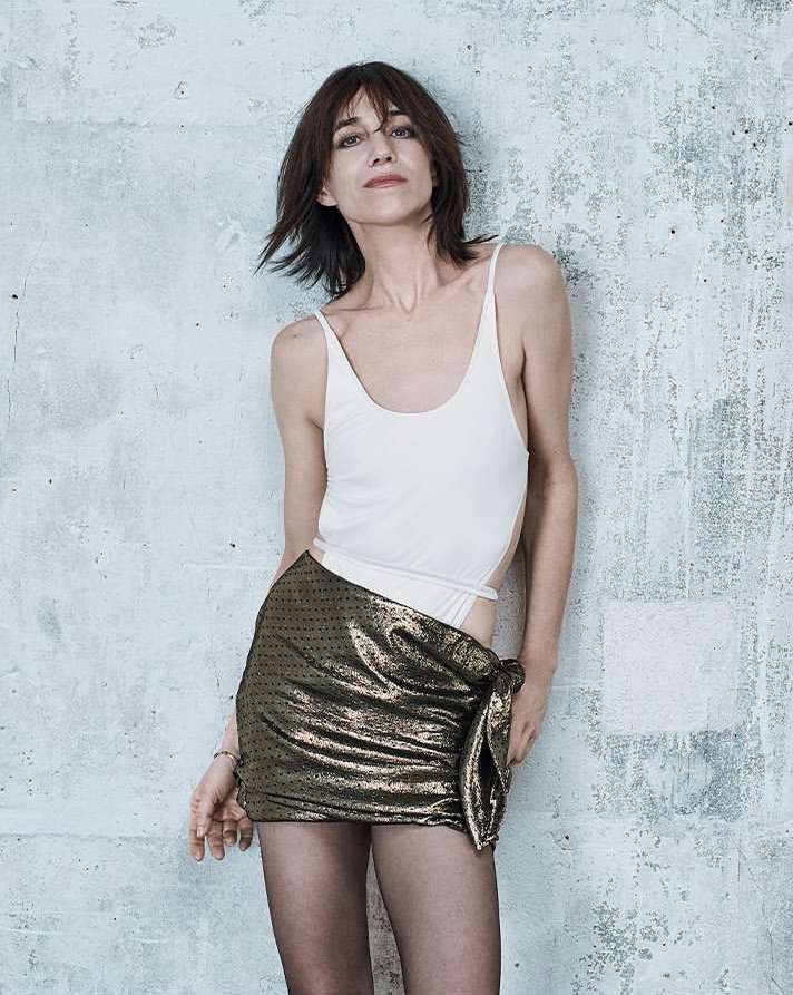 Françoise Hardy wearing a white bodysuit and gold mini skirt against a concrete wall photographed by Paola Kudacki