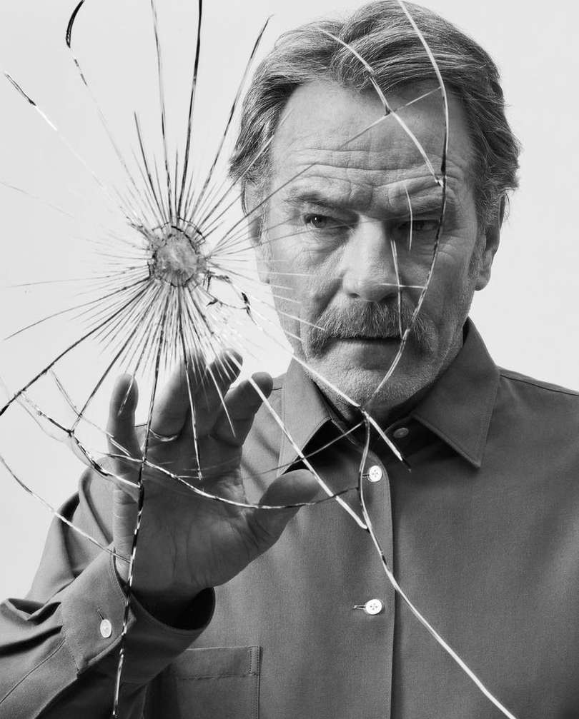 Black and white portrait of a mature man with mustache, reaching toward a cracked glass surface, captured in a medium close-up.