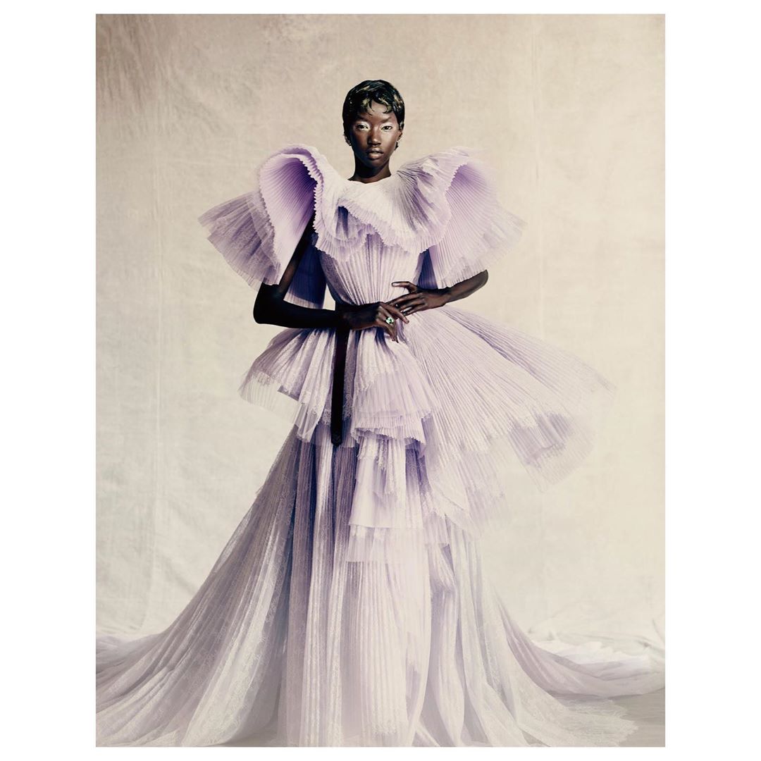 Elegant Black woman in a light purple, ruffled high-fashion gown poses in a studio setting, creating a striking and sophisticated portrait.