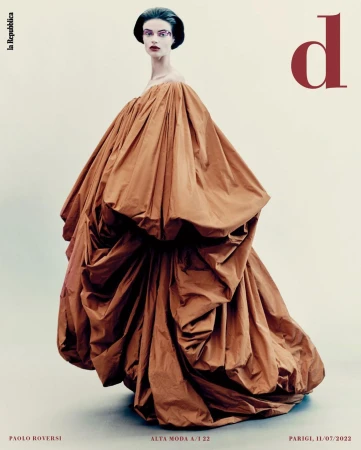 Model in voluminous brown off-the-shoulder dress with dark sculptural updo against a seamless pale grey background by Paolo Roversi