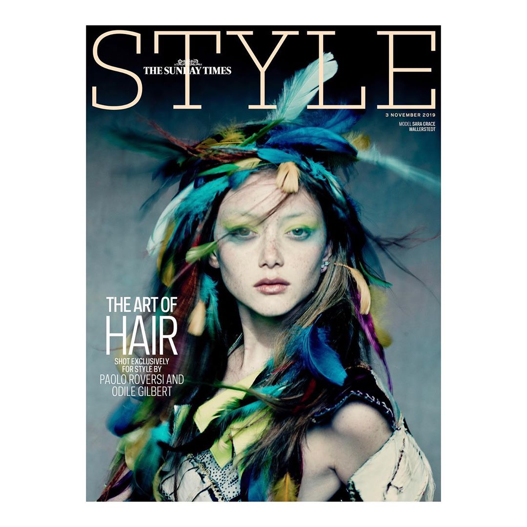Magazine cover featuring a woman with vibrant feather headdress, artistic makeup, and fashion-forward styling, against a muted background.