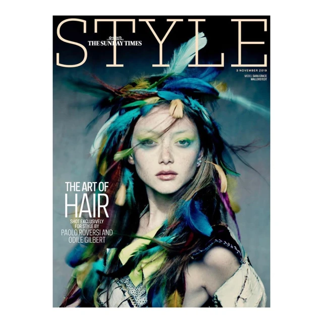 Magazine cover featuring a woman with vibrant feather headdress, artistic makeup, and fashion-forward styling, against a muted background.