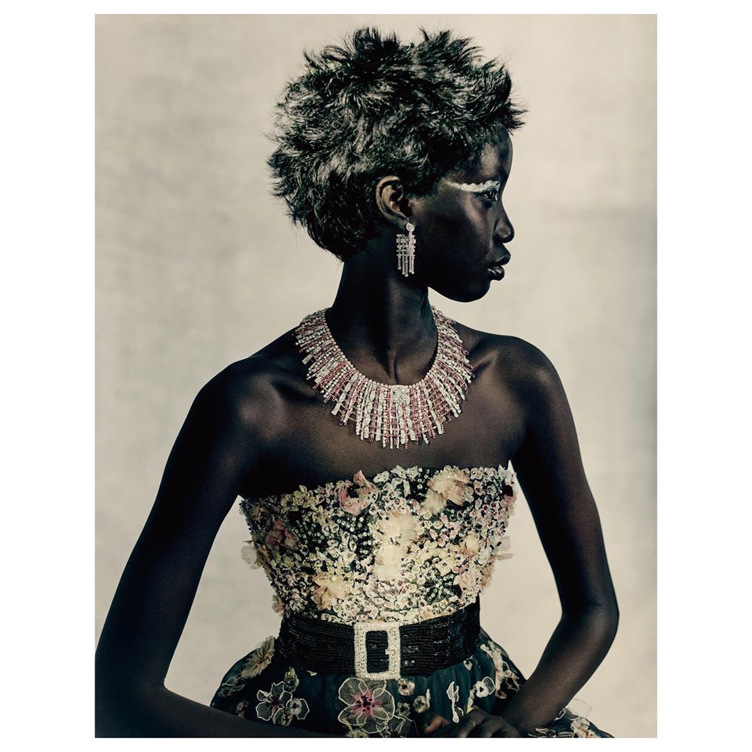 Striking studio portrait of an African woman with a short grey hairstyle, wearing a floral dress and necklace, gazing to the side.