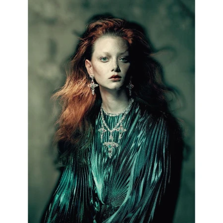 Elegant woman with red hair poses in a draped green dress and cross jewelry in a studio, showcasing a fashion and beauty aesthetic.