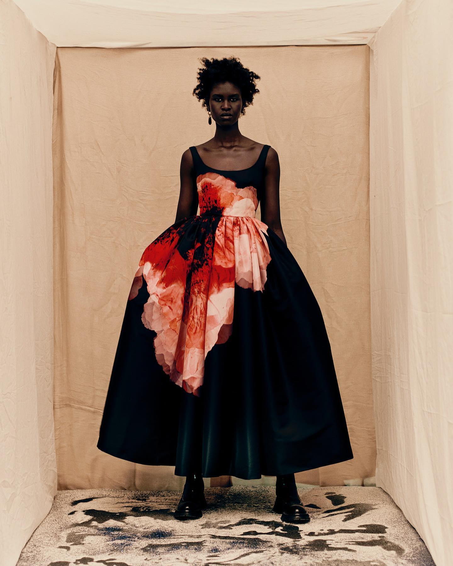 An African-American female model poses in a photo studio wearing a black and floral-print dress and black boots for a fashion editorial.