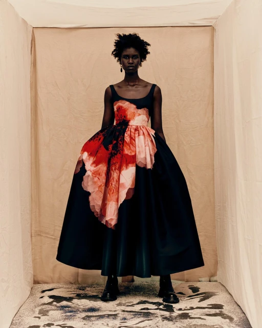 An African-American female model poses in a photo studio wearing a black and floral-print dress and black boots for a fashion editorial.