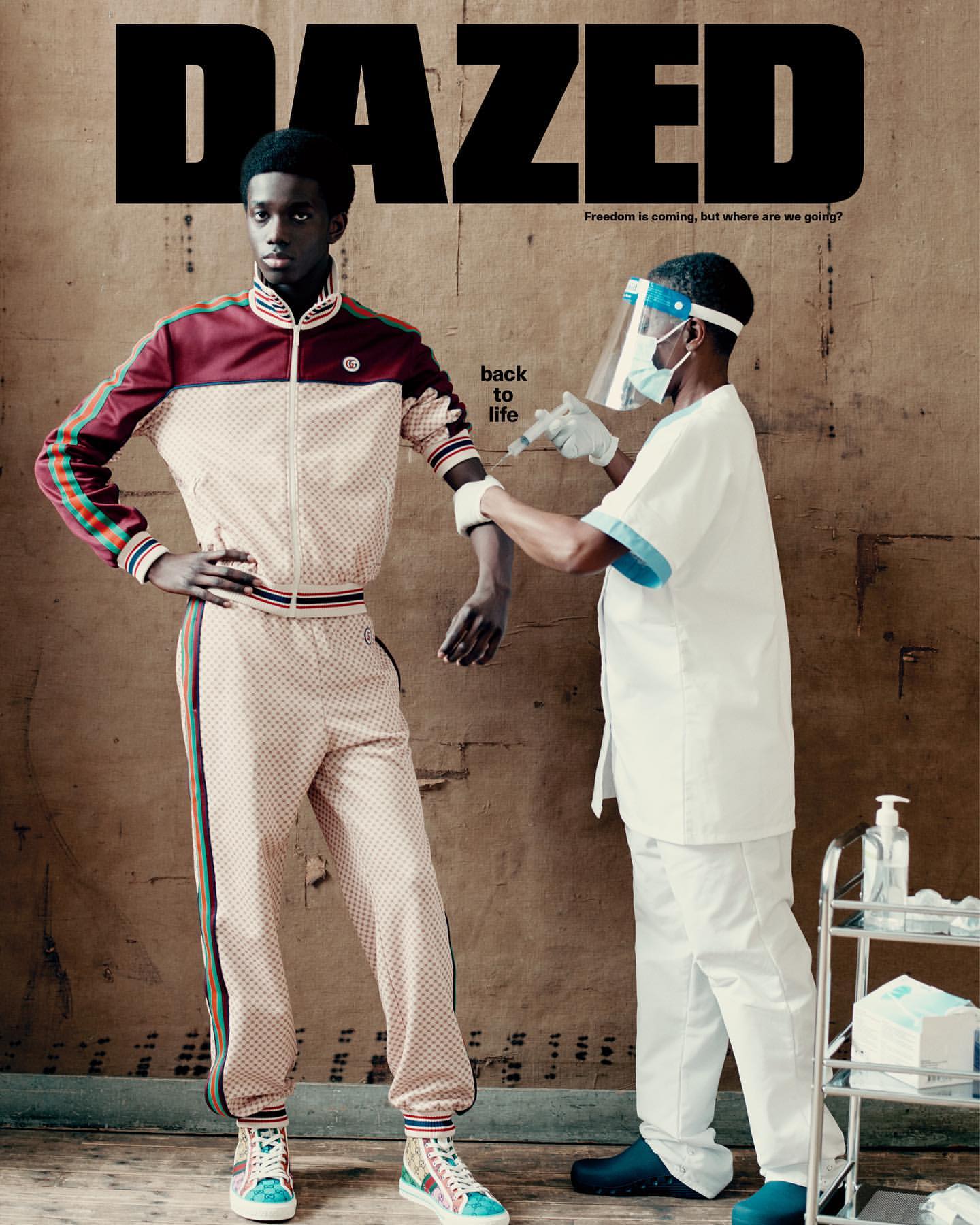 Dazed magazine cover featuring a model in a tracksuit receiving a vaccination from a medical professional in protective gear indoors.