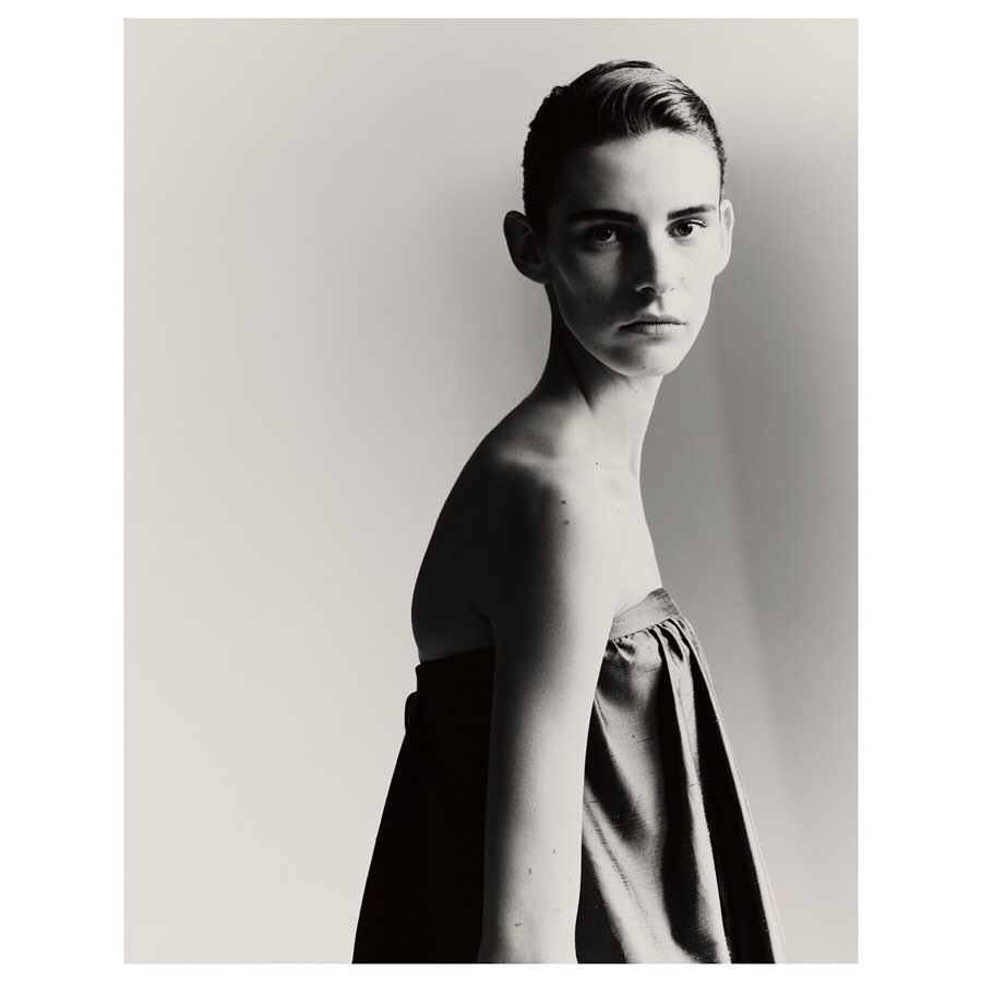 Monochromatic portrait of a young adult female model with short hair in draped fabric against a pale background, fashion or beauty editorial.