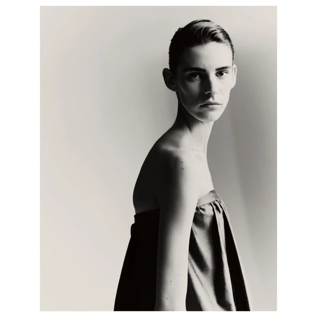 Monochromatic portrait of a young adult female model with short hair in draped fabric against a pale background, fashion or beauty editorial.