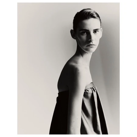Monochromatic portrait of a young adult female model with short hair in draped fabric against a pale background, fashion or beauty editorial.