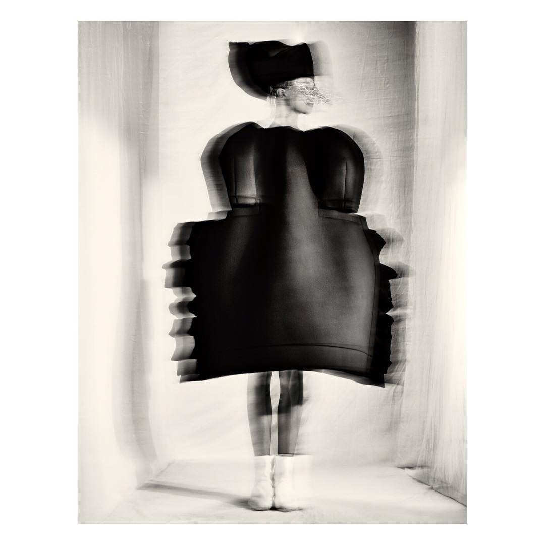 Abstract fashion photograph of an adult female wearing a black dress and hat, posed in an indoor setting with blurred motion effect.