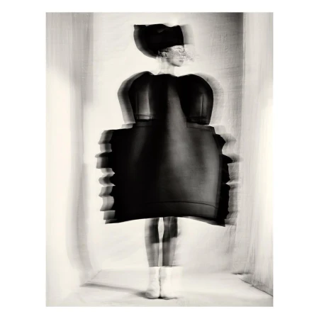 Abstract fashion photograph of an adult female wearing a black dress and hat, posed in an indoor setting with blurred motion effect.