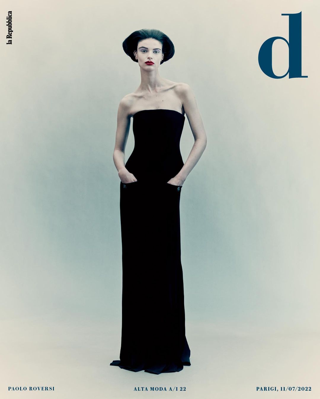 Elegant fashion magazine cover featuring a slender model in a black strapless gown and formal headwear on a pale background.