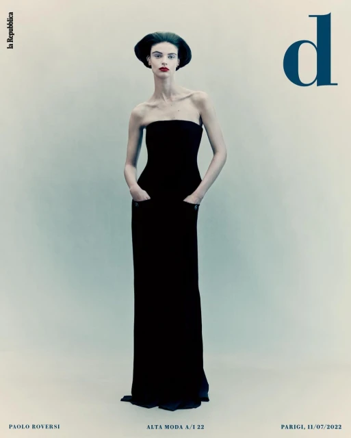 Elegant fashion magazine cover featuring a slender model in a black strapless gown and formal headwear on a pale background.