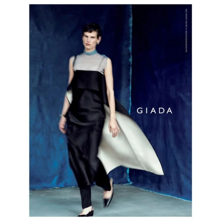 Model in black and grey layered dress with flowing cape walking against a textured blue backdrop