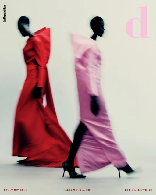 Two figures in flowing gowns, one red, one pink, blurred in motion against a pale backdrop, evoke high fashion editorial photography.