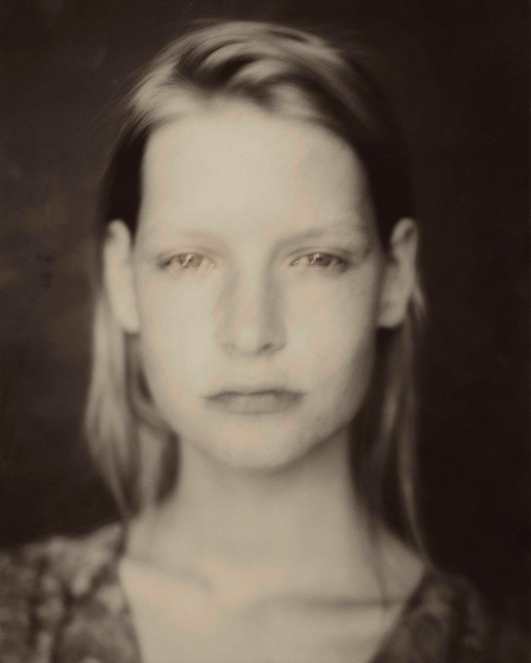 Portrait of a woman with long hair looking directly at the camera in a soft-focus sepia-toned vintage style.