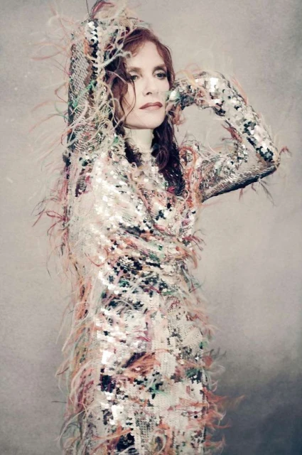 Adult female poses in a sequined dress with feathers, indoor, photo studio backdrop, portrait framing, looking away from the camera.