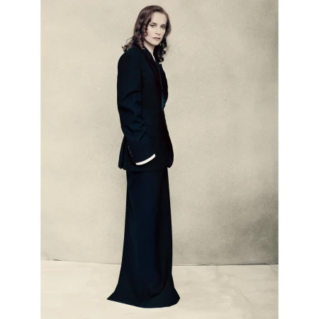 Portrait of a woman wearing a black suit jacket and long skirt standing against a neutral studio backdrop