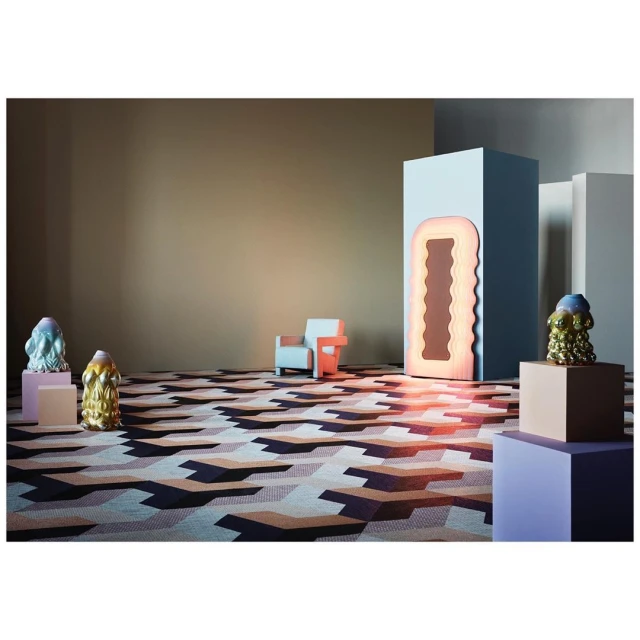 Geometric pattern carpet in modern room with sculptural objects, art installation, and pastel chair against a neutral backdrop.