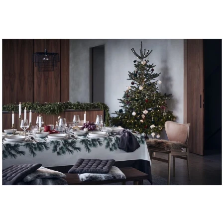 Christmas table setting with fir branch tablecloth, decorations, candles, dinnerware, and brown chair with fur seat in a dining room.