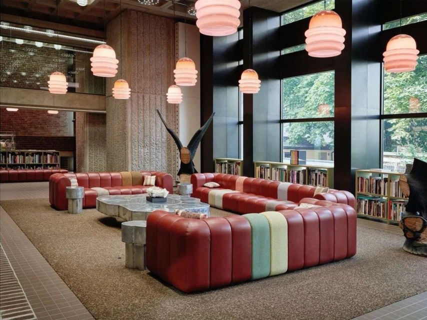 Spacious modern library interior with red upholstered sofas, metal coffee table, and numerous pendant lights illuminating bookshelves.