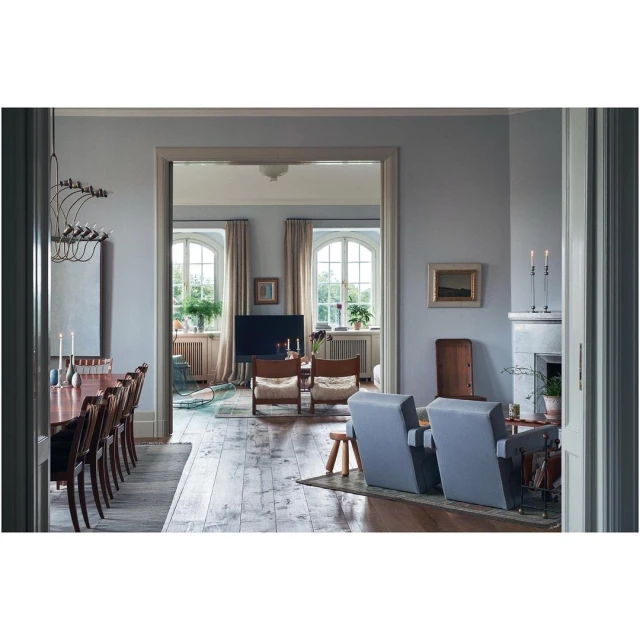 Living room interior with wooden floors, grey walls, natural light from windows, and a mix of modern and vintage furniture.