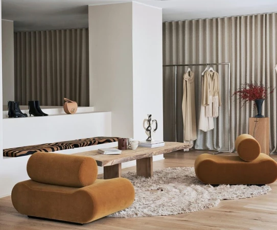 Interior design of a minimalist living room featuring a wooden coffee table, armchairs, a clothing rack, and neutral color palette.