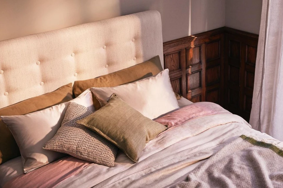 Bedroom interior with upholstered headboard, decorative pillows, and a cozy blanket on a neatly made bed next to paneled wall.