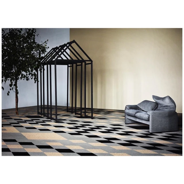 Interior with a gray modern couch, a black architectural frame, and a tree on a geometric patterned floor in front of a light wall.