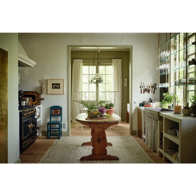 Interior view of a rustic kitchen featuring a wooden table with produce, a vintage stove, and natural light from a window.