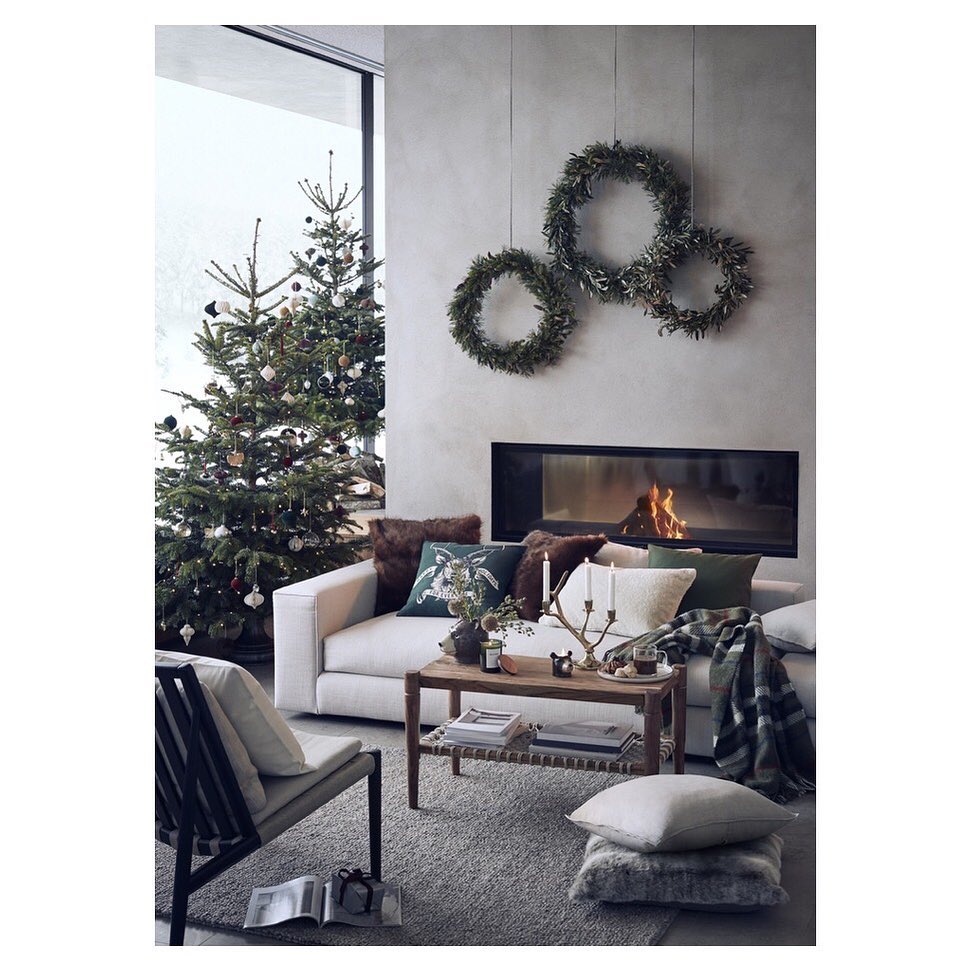 Christmas tree and wreaths decorate a living room interior with a sofa, coffee table, chair, and fireplace.
