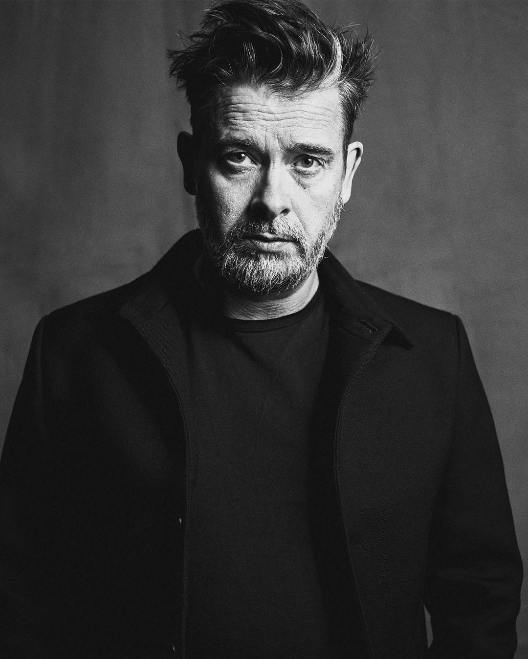 Monochrome portrait of a man in his 40s wearing a dark jacket against a dark textured background photographed by Pär Olofsson.