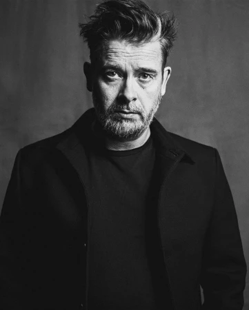 Monochrome portrait of a man in his 40s wearing a dark jacket against a dark textured background photographed by Pär Olofsson.