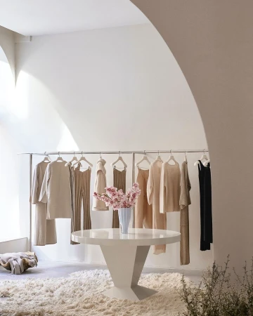 Clothing boutique interior with a round white table holding a vase of pink flowers, a rack of clothes, and a shag carpet.