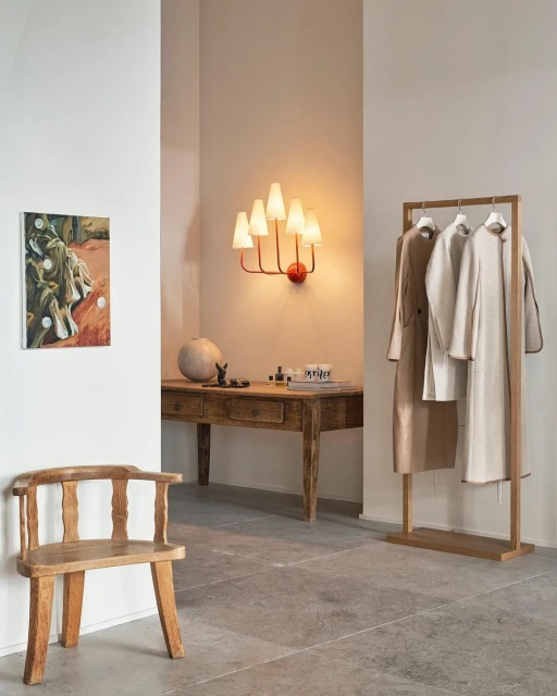 Interior with a wooden chair, wooden table, coats on a rack, and a painting on the wall, creating a cozy and artful living space.