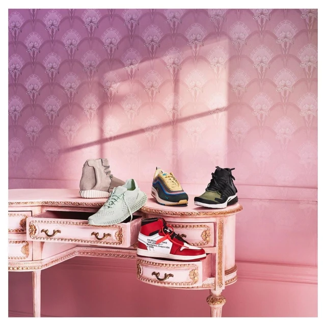 Five fashion sneakers displayed on a pink vanity against a pink-patterned wall, illuminated by soft light, showcasing a modern shoe collection.
