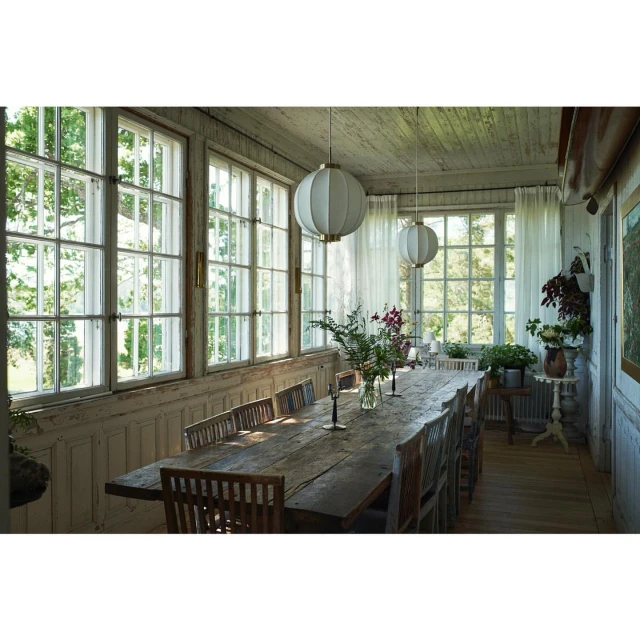 Rustic dining room with long wooden table, globe pendant lights, and large windows overlooking greenery, creating a bright and airy atmosphere.