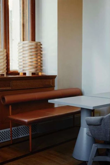 Interior view features a brown leather bench in front of a window with a wooden frame, alongside a gray table and chair.