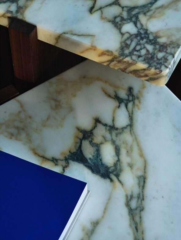 Close-up showcasing two marble tables with unique patterns, accompanied by a deep blue book in a minimalist, elegant composition.
