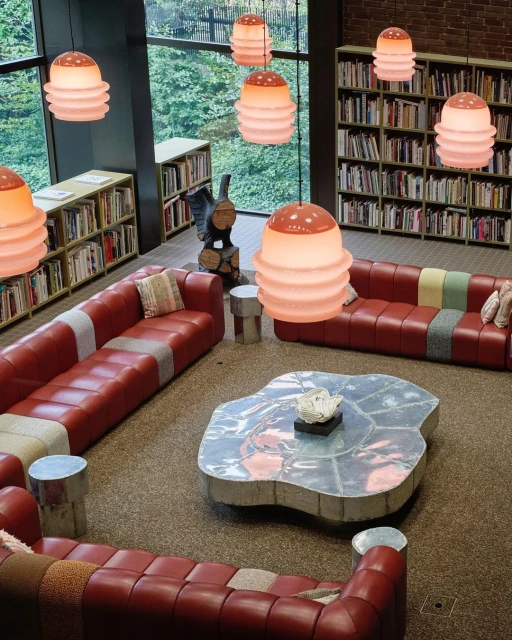 Library interior featuring red sectional sofas, a custom metal coffee table, bookcases filled with books, and modern pendant lighting.