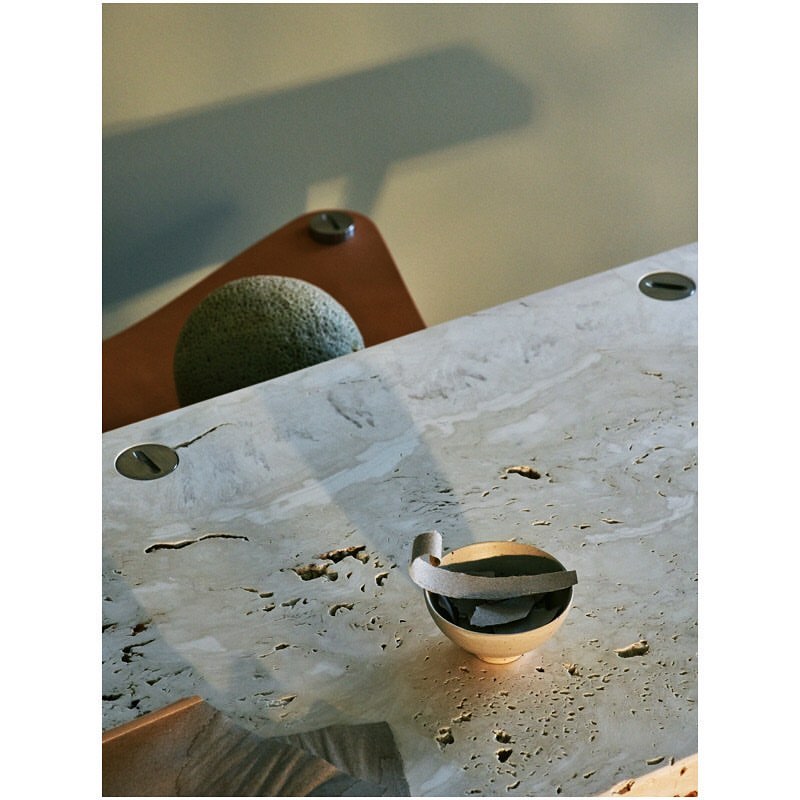 Minimalist interior scene featuring a round stone object on a wooden surface, a small bowl, and a travertine stone table.