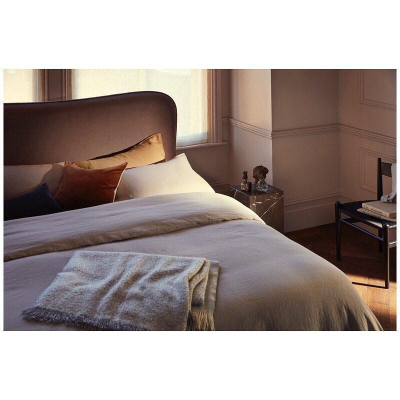 Bedroom interior featuring a made bed with a cozy blanket, headboard with decorative pillows, a side table, and a stylish chair.
