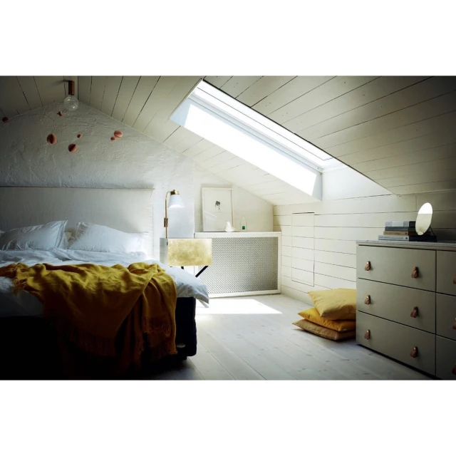 Bedroom interior featuring a bed with a yellow blanket, dresser with mirror, and a window letting in natural light in an attic setting.