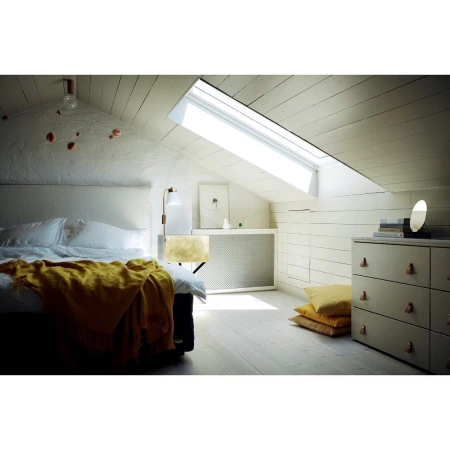 Bedroom interior featuring a bed with a yellow blanket, dresser with mirror, and a window letting in natural light in an attic setting.