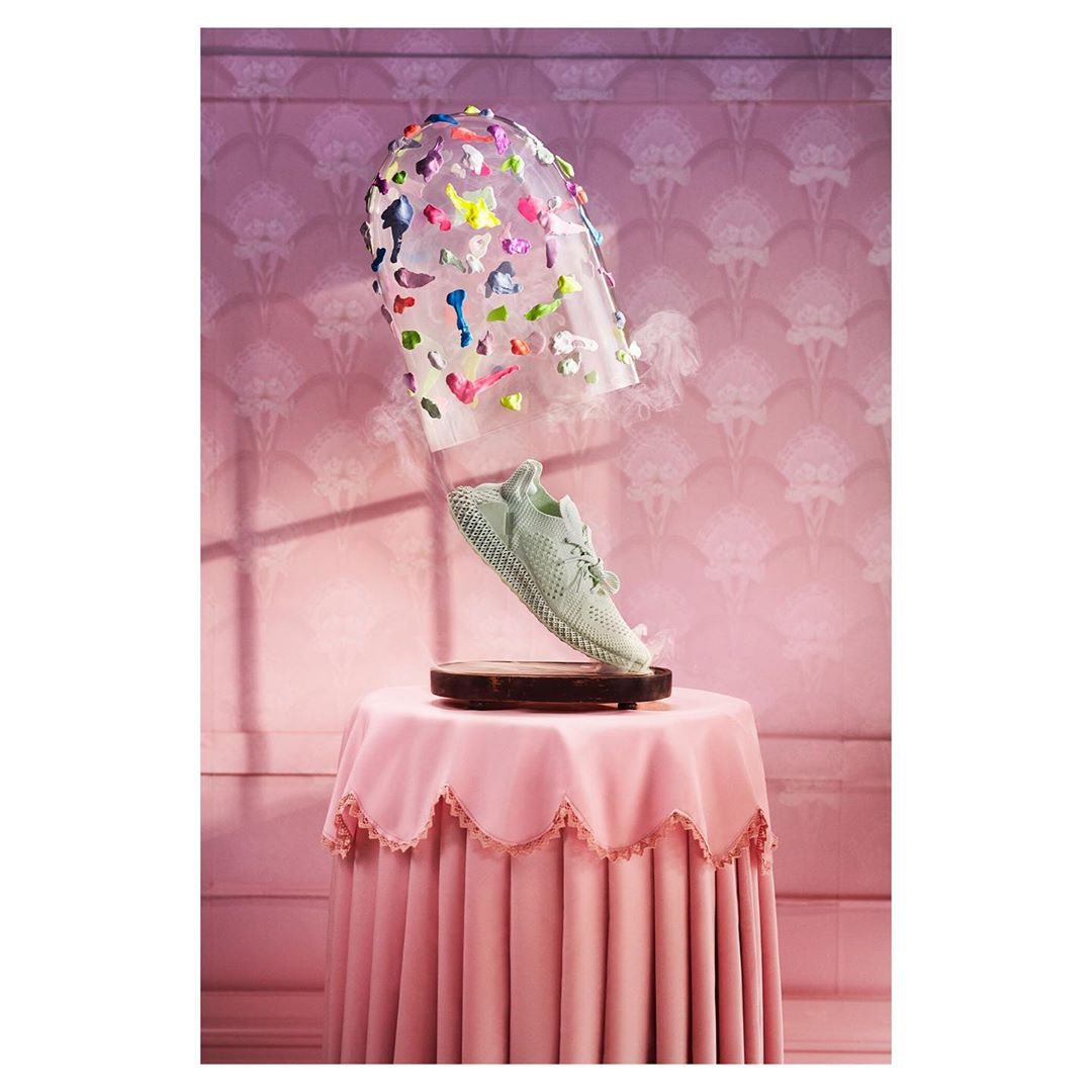 Conceptual image of a light green sneaker displayed on a small table under a transparent plastic dome with colorful accents.